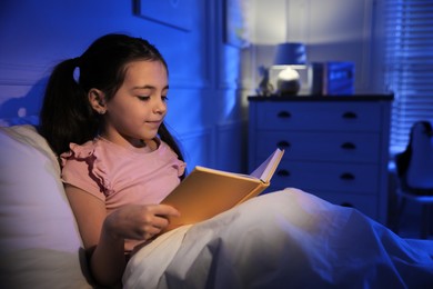 Photo of Little girl reading fairy tale in dark bedroom
