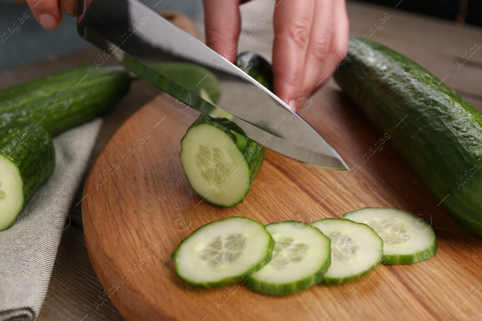 Photo of Woman cutting cucumber on wooden board at table, closeup