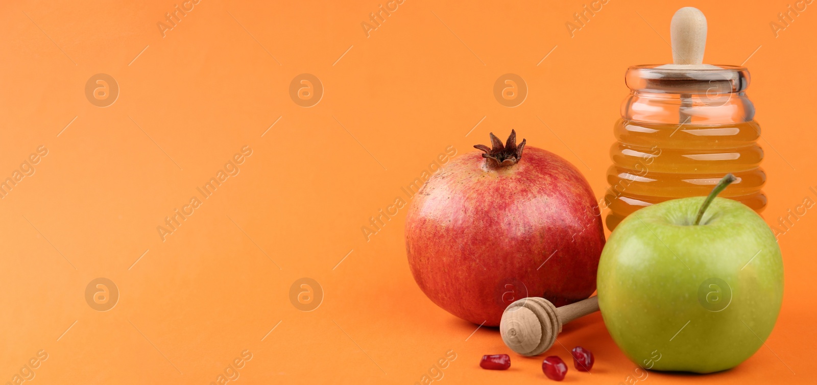 Photo of Honey, apples and pomegranate on orange background, space for text. Rosh Hashanah holiday