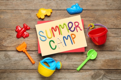 Photo of Text SUMMER CAMP made of modelling clay and different sand molds on wooden table, flat lay