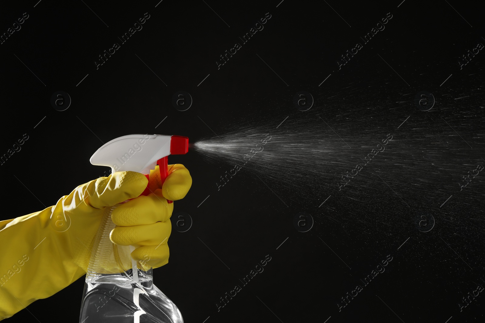 Photo of Woman spraying liquid from bottle on black background, closeup