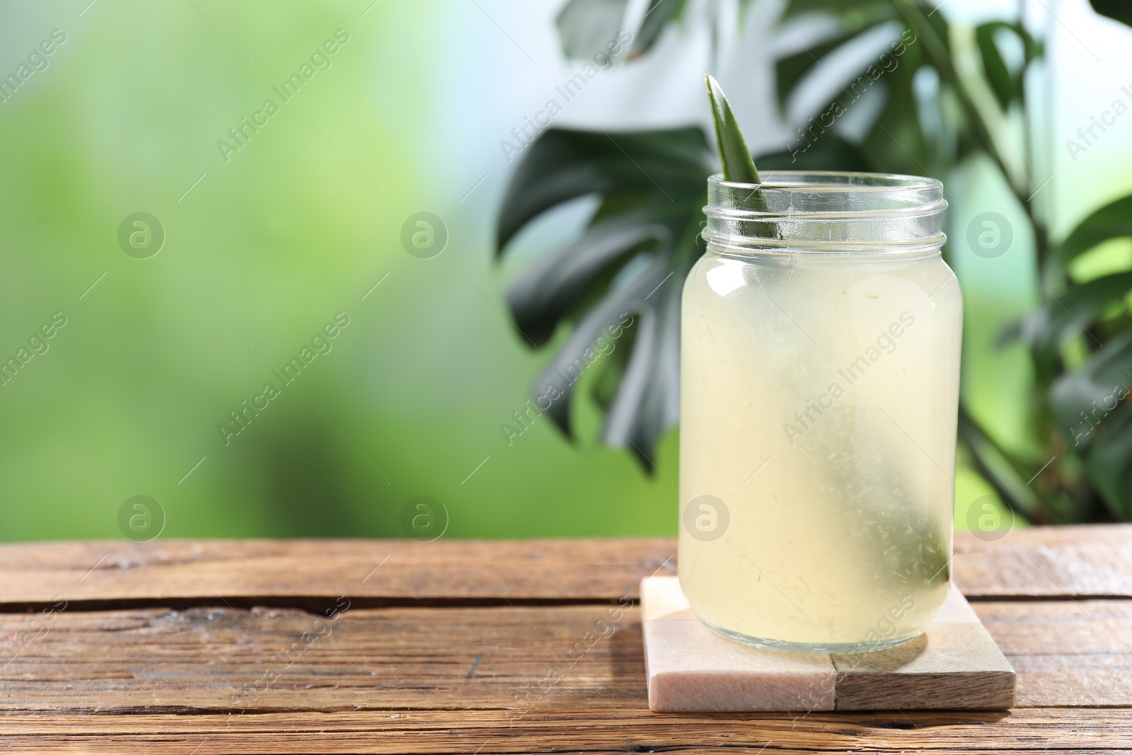 Photo of Fresh aloe juice in jar on wooden table outdoors, space for text