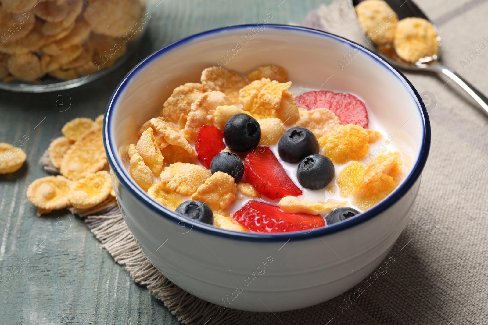 Photo of Delicious crispy cornflakes with milk and fresh berries on light blue wooden table, closeup