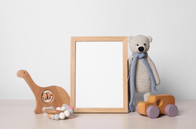 Photo of Empty square frame and different toys on white wooden table