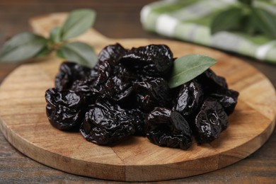 Photo of Tasty dried prunes and green leaf on wooden table, closeup