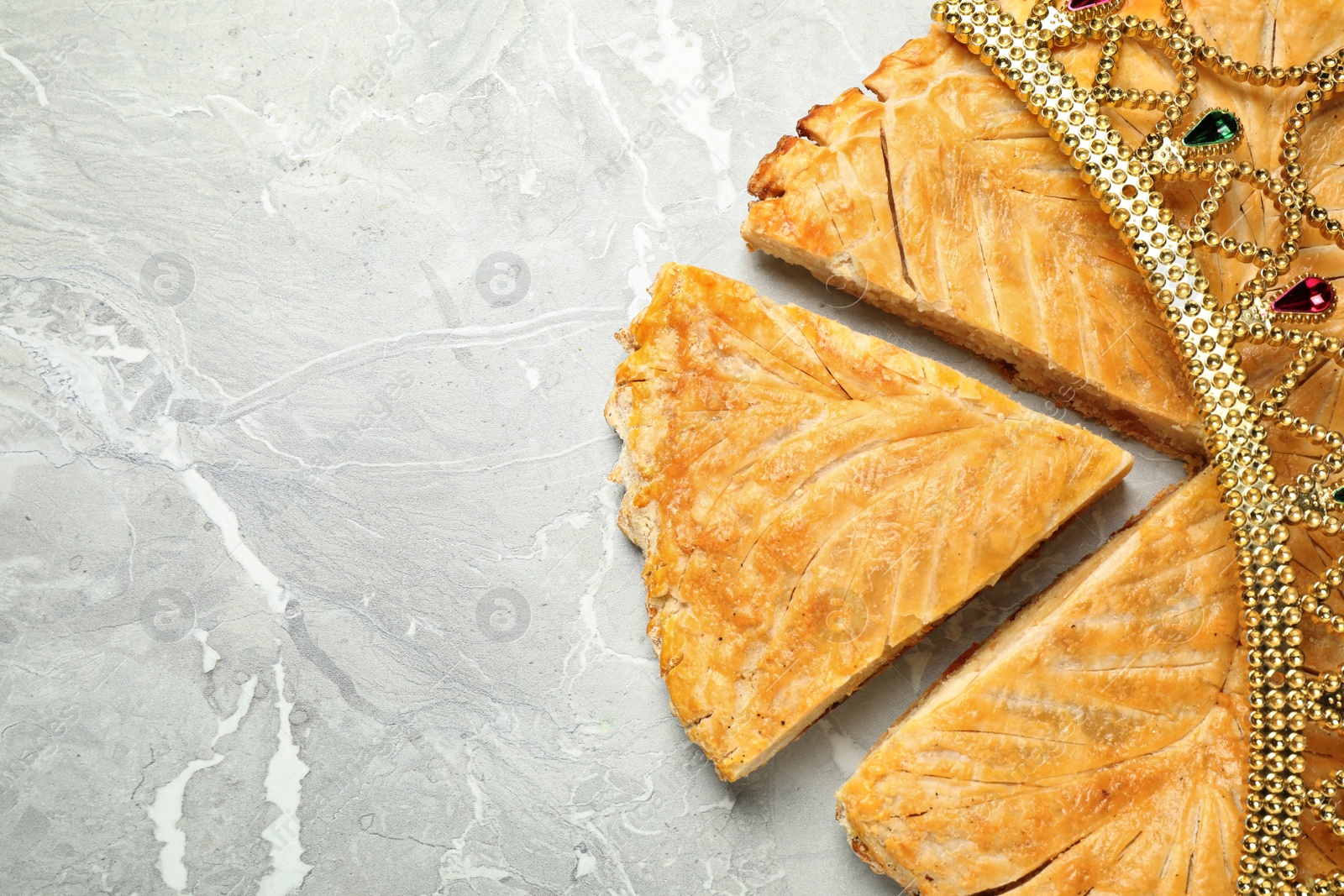 Photo of Traditional galette des Rois with decorative crown on grey marble table, flat lay. Space for text