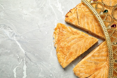 Photo of Traditional galette des Rois with decorative crown on grey marble table, flat lay. Space for text