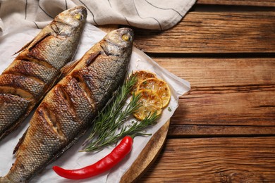 Photo of Delicious baked sea bass fish and ingredients on wooden table. Space for text