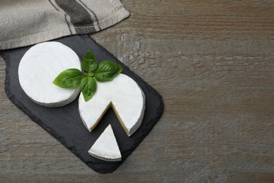 Photo of Tasty cut and whole brie cheeses with basil on wooden table, flat lay. Space for text
