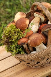 Photo of Wicker basket with fresh wild mushrooms on wooden table outdoors, closeup