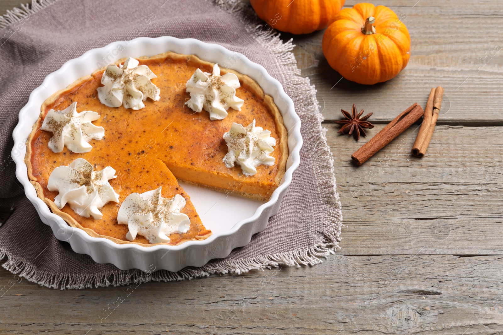 Photo of Delicious pie with pumpkins, whipped cream and spices on wooden table, space for text