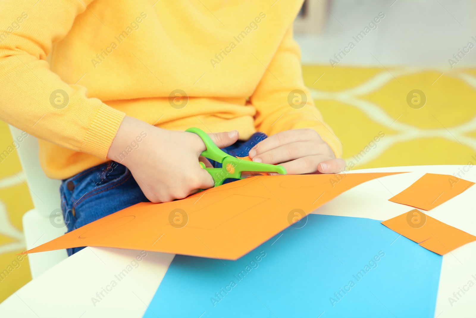 Photo of Boy cutting orange paper at desk in room, closeup. Home workplace