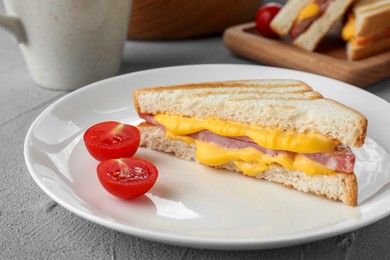 Tasty sandwich with ham, melted cheese and tomatoes on grey textured table, closeup