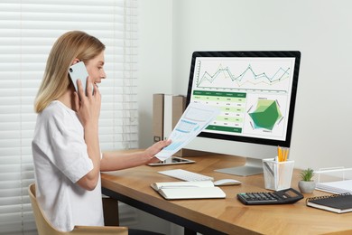 Professional accountant talking on phone while working at wooden desk in office