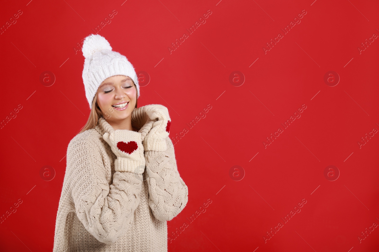 Photo of Young woman in warm sweater, mittens and hat on red background, space for text. Winter season