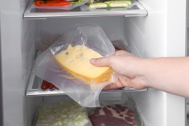 Photo of Woman putting vacuum bag with cheese into fridge, closeup. Food storage