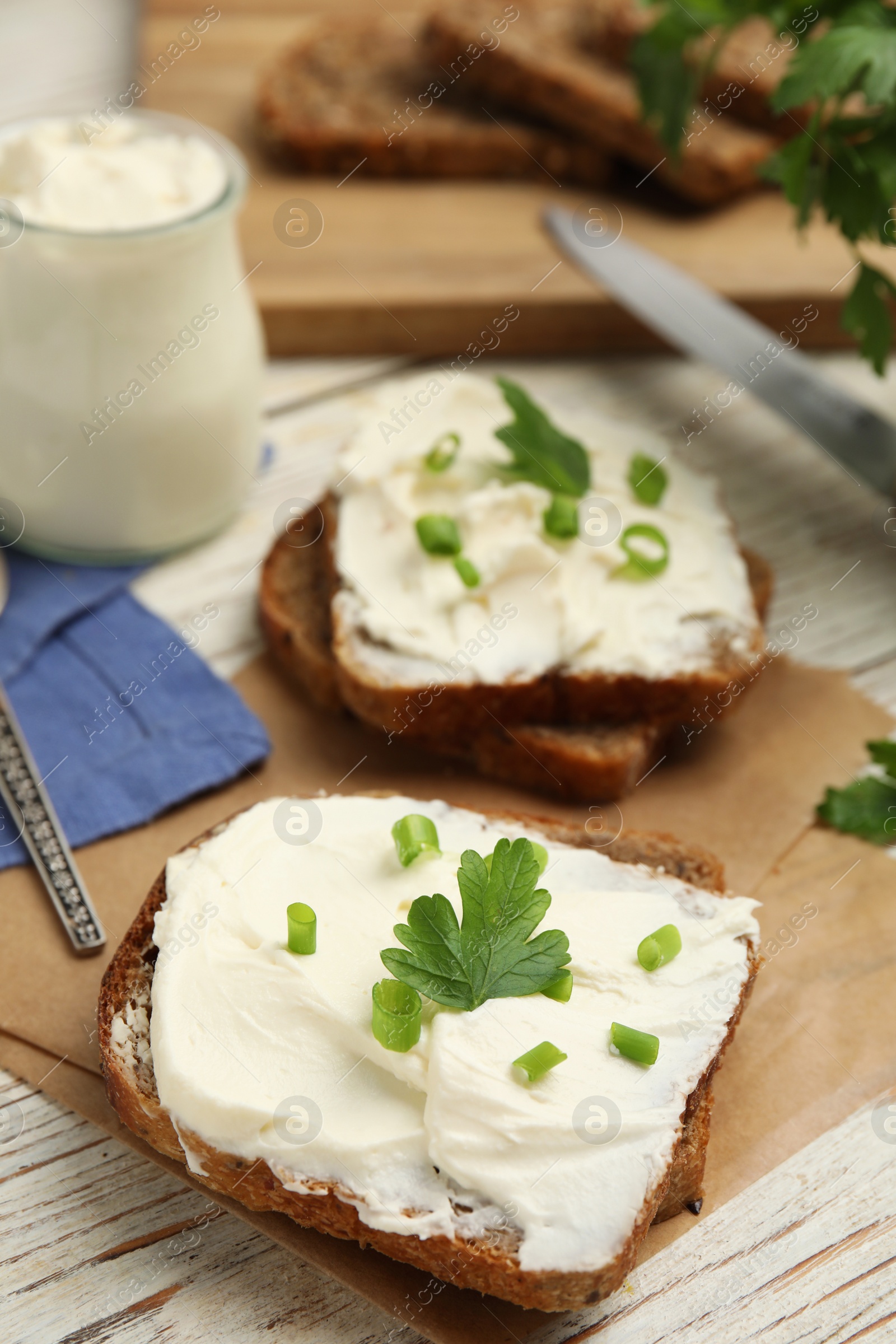 Photo of Bread with cream cheese, green onion and parsley on white wooden table