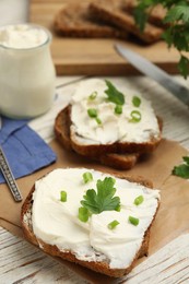 Photo of Bread with cream cheese, green onion and parsley on white wooden table