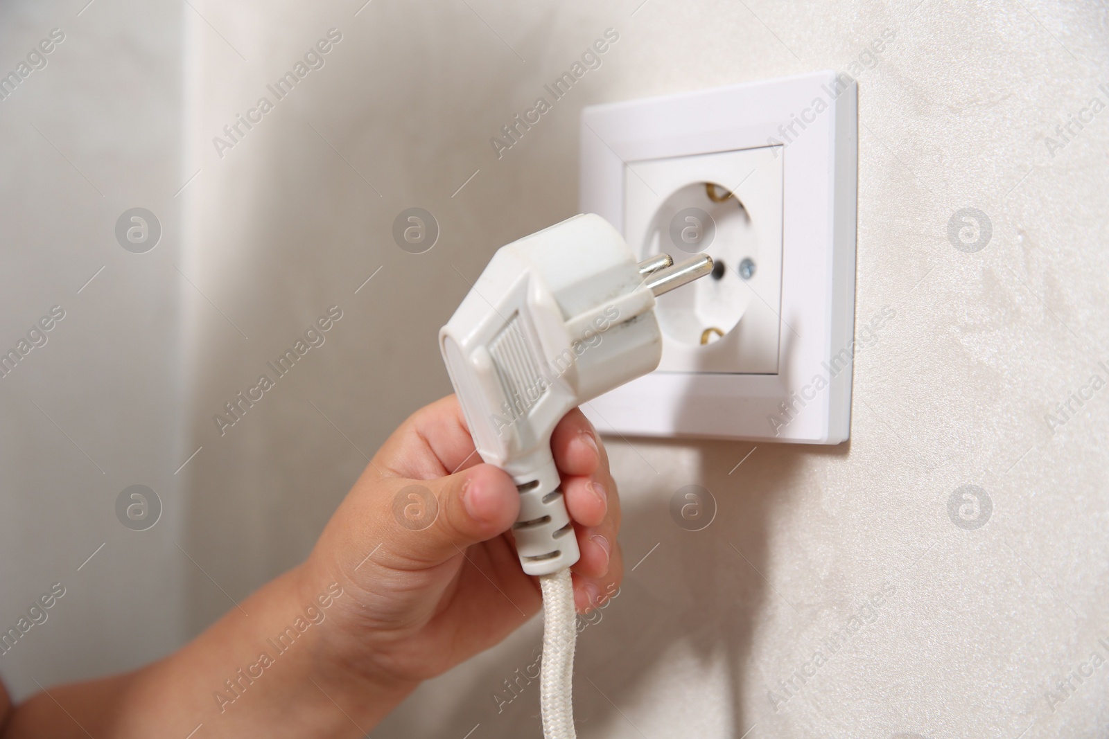 Photo of Little child playing with electrical socket and plug indoors, closeup. Dangerous situation