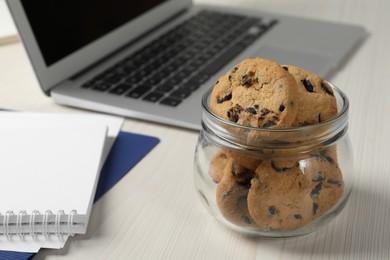 Jar with chocolate chip cookies on white wooden table in office, closeup. Space for text