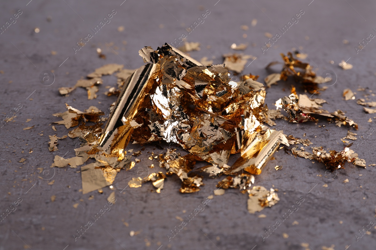 Photo of Many pieces of edible gold leaf on grey textured table, closeup