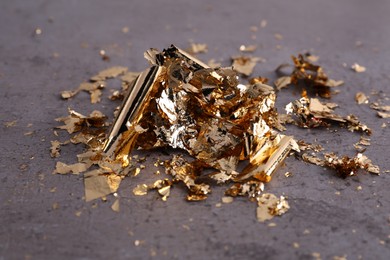 Photo of Many piecesedible gold leaf on grey textured table, closeup