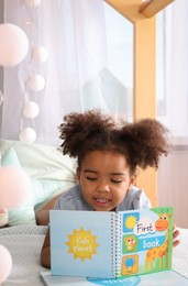 African American girl reading book on bed at home