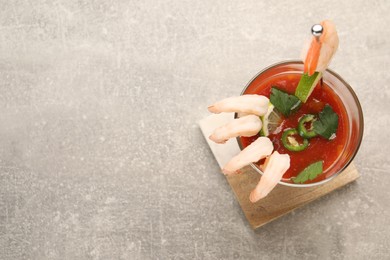 Photo of Tasty shrimp cocktail with sauce, parsley and lime in glass on light grey table, top view. Space for text