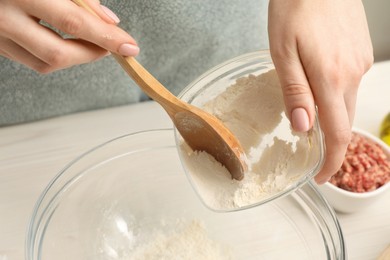 Woman putting flour into bowl at white wooden table, closeup