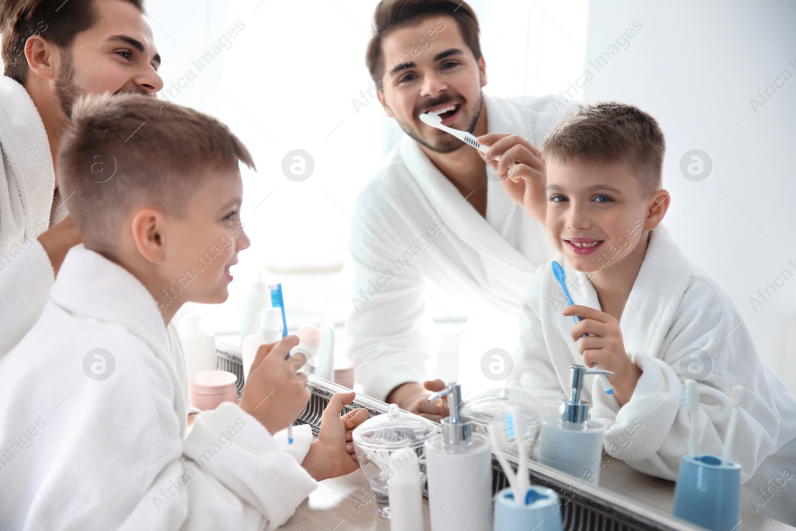 Photo of Young man and his son with toothbrushes near mirror in bathroom. Personal hygiene