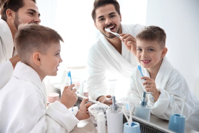 Photo of Young man and his son with toothbrushes near mirror in bathroom. Personal hygiene