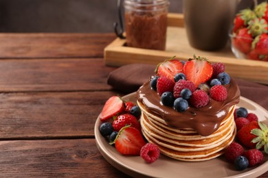 Stack of tasty pancakes with fresh berries and chocolate spread on wooden table, space for text