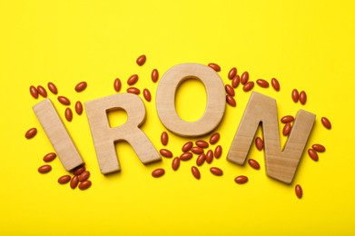 Photo of Word Iron and pills on yellow background, flat lay. Anemia treatment