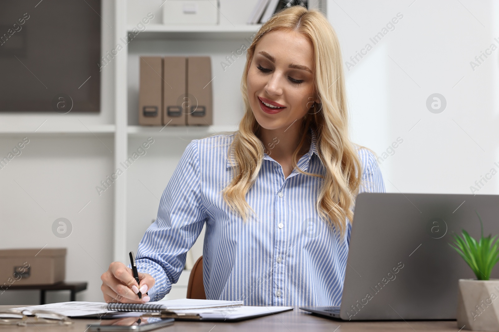 Photo of Happy secretary taking notes at table in office