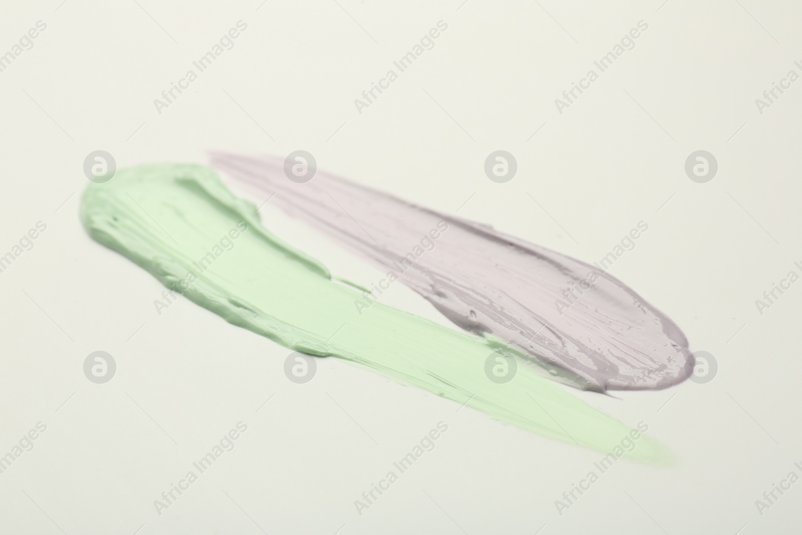 Photo of Strokes of green and purple color correcting concealers on white background