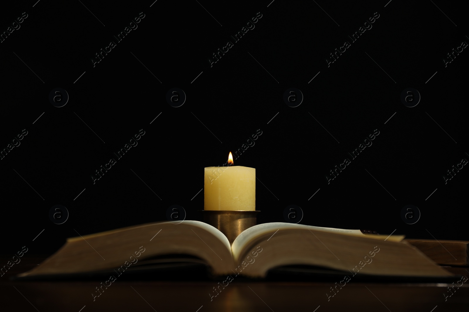 Photo of Church candle and Bible on table against black background