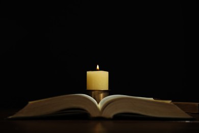 Photo of Church candle and Bible on table against black background