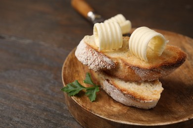 Photo of Tasty butter curls and slices of bread on wooden table, closeup. Space for text