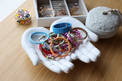 Photo of Ceramic hand stand with many stylish bracelets and jewelry boxes on wooden table