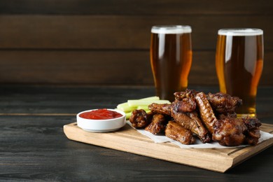 Photo of Delicious chicken wings served with beer on black wooden table