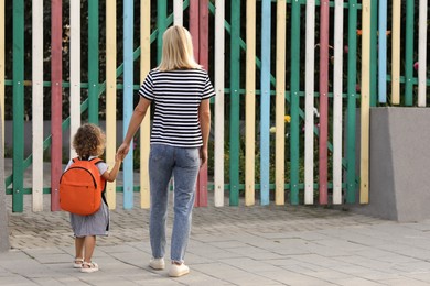 Photo of Woman and her little daughter on their way to kindergarten outdoors, back view. Space for text