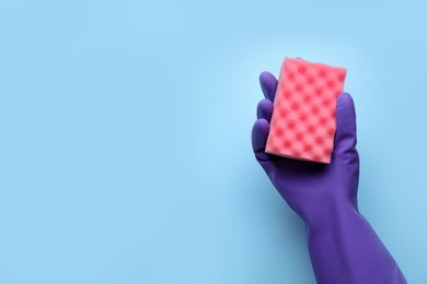 Woman in rubber glove holding sponge on light blue background, top view. Space for text