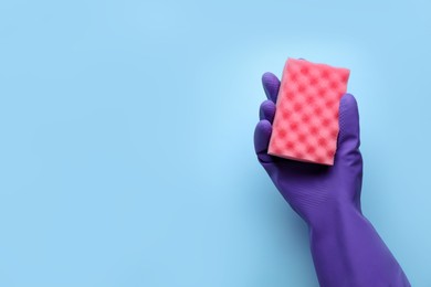 Photo of Woman in rubber glove holding sponge on light blue background, top view. Space for text