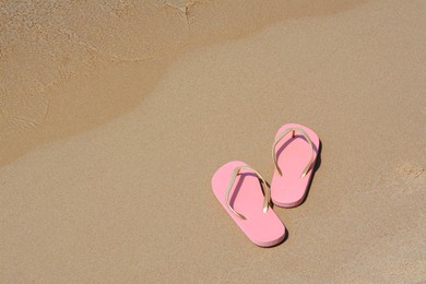 Stylish pink flip flops on wet sand near sea, space for text