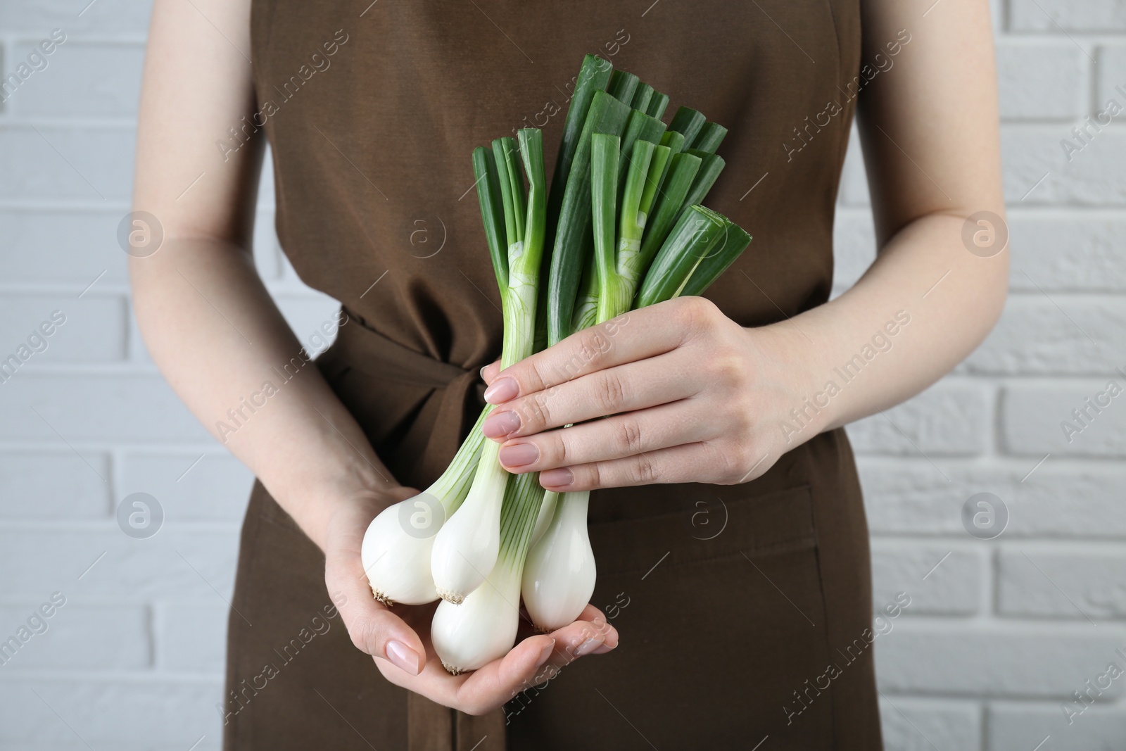 Photo of Woman holding green spring onions near white brick wall, closeup