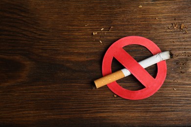 Photo of Cigarette with prohibition sign and space for text on wooden table, top view. Quitting smoking concept