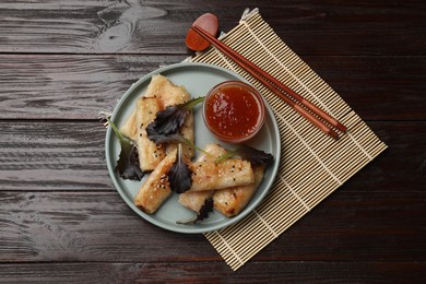 Photo of Tasty fried spring rolls, lettuce and sauce on wooden table, top view