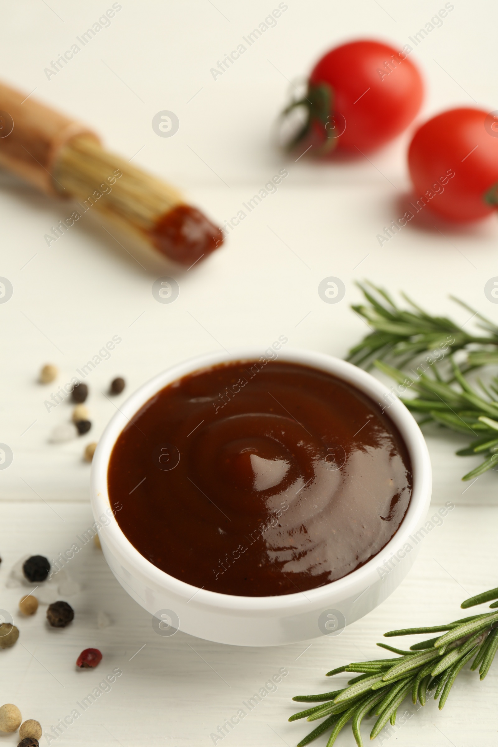 Photo of Tasty barbeque sauce in bowl, rosemary and spices on white wooden table