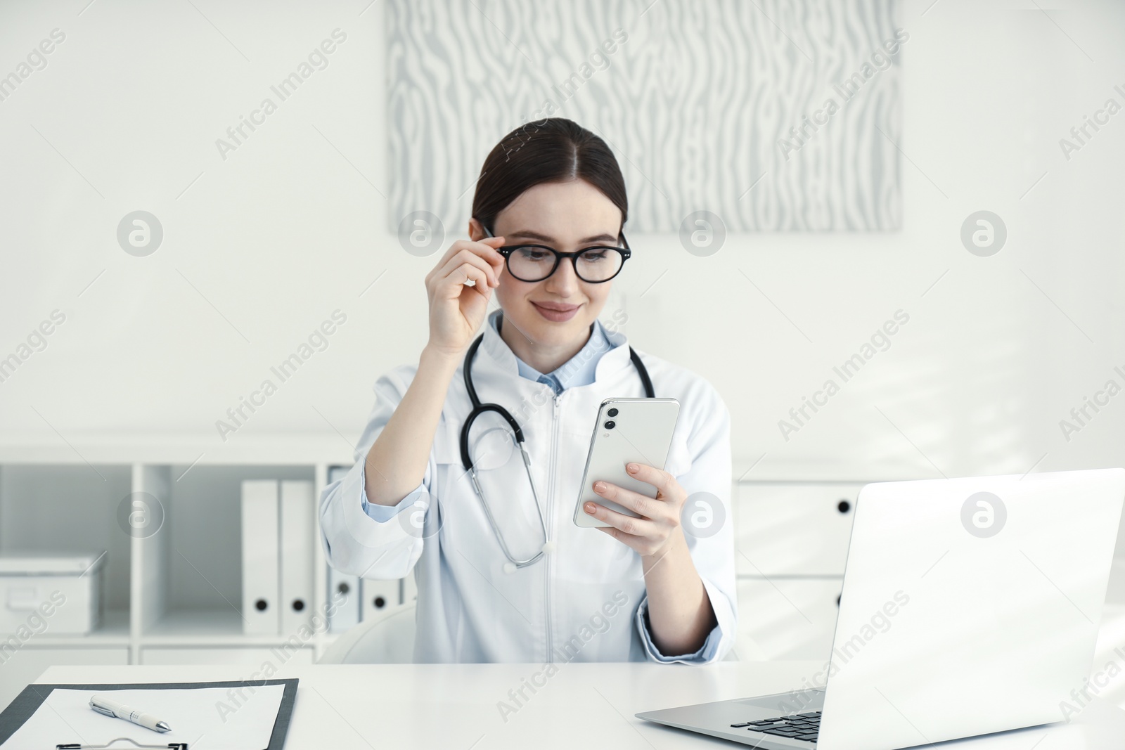 Photo of Young female doctor with smartphone at table in office
