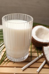 Photo of Glass of delicious vegan milk, coconuts and leaf on table, closeup